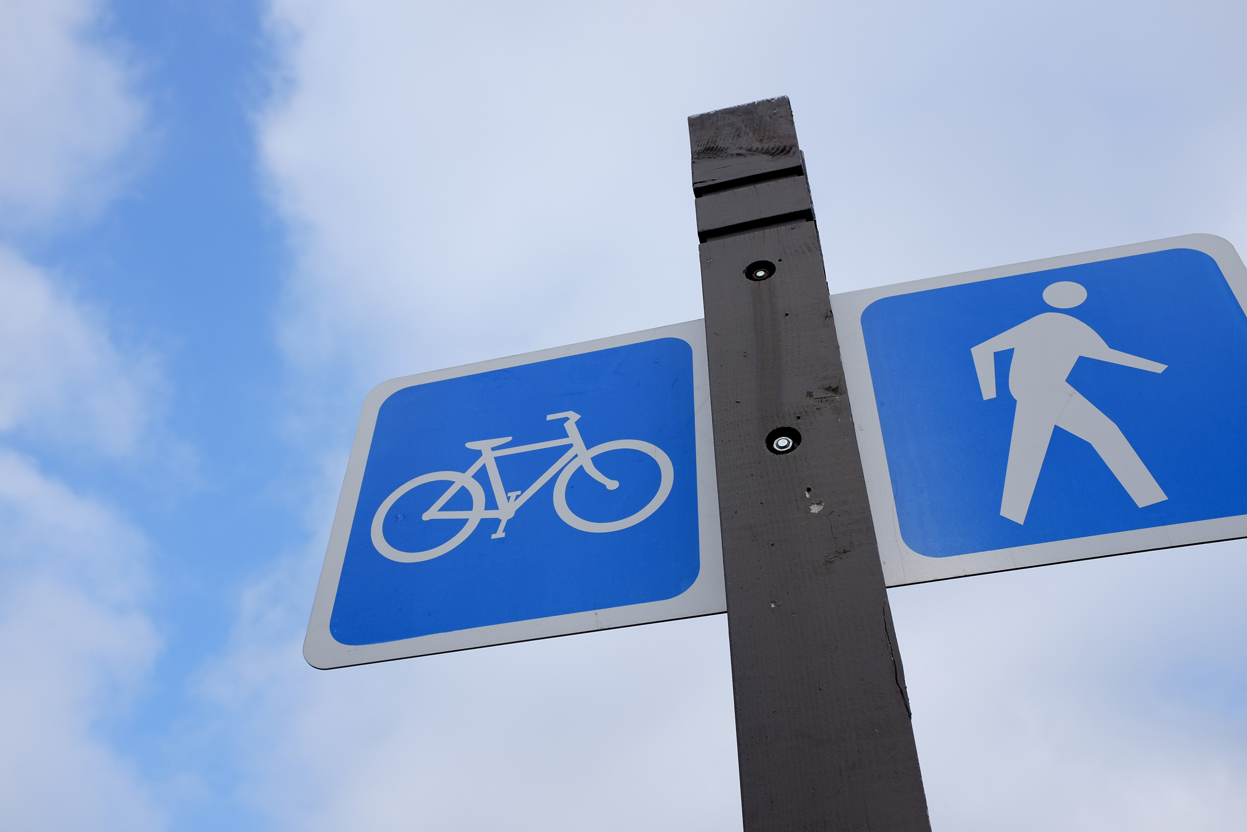 Biking and walking trail signs against a partially cloudy sky